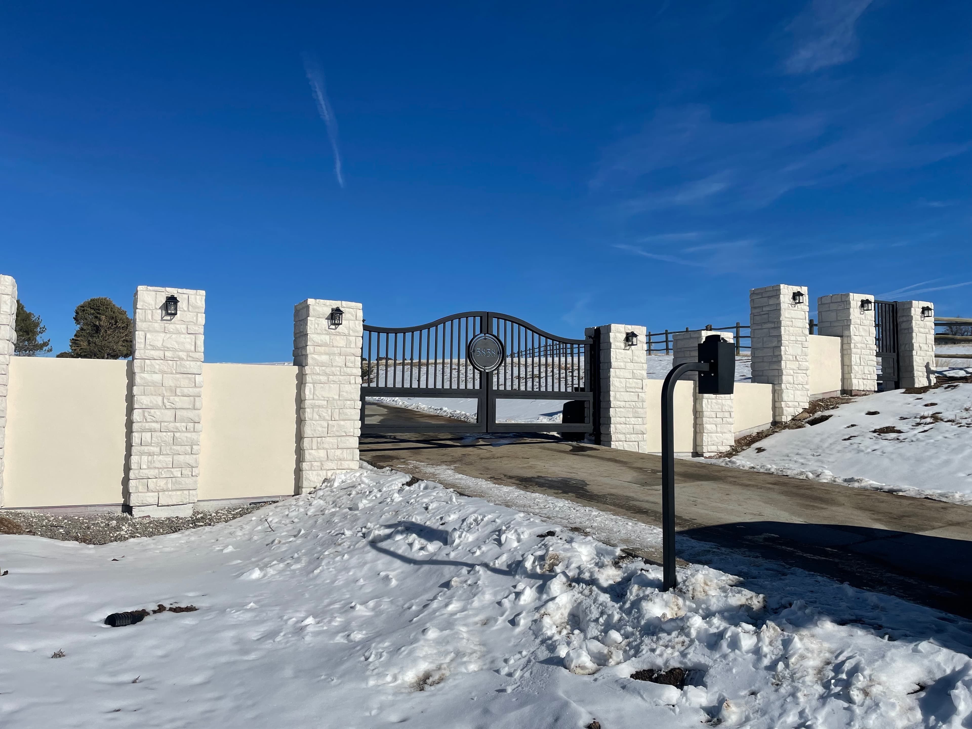 Custom ornamental iron automated swing gate with decorative stone columns in Genesee, CO